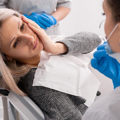 Woman in dental chair looking at dentist holding hand to sore cheek