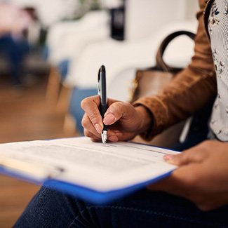 Hands filling out forms on blue clipboard in waiting room