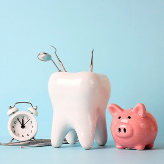 Model tooth with dental instruments next to clock and pink piggy bank with light blue background