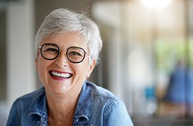 Senior woman with glasses and denim jacket smiling
