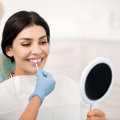 Female dental patient with handheld mirror having teeth shade matched