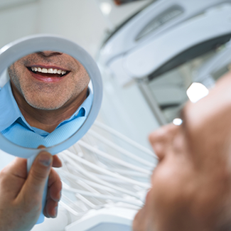 Man in dental chair checking smile in mirror